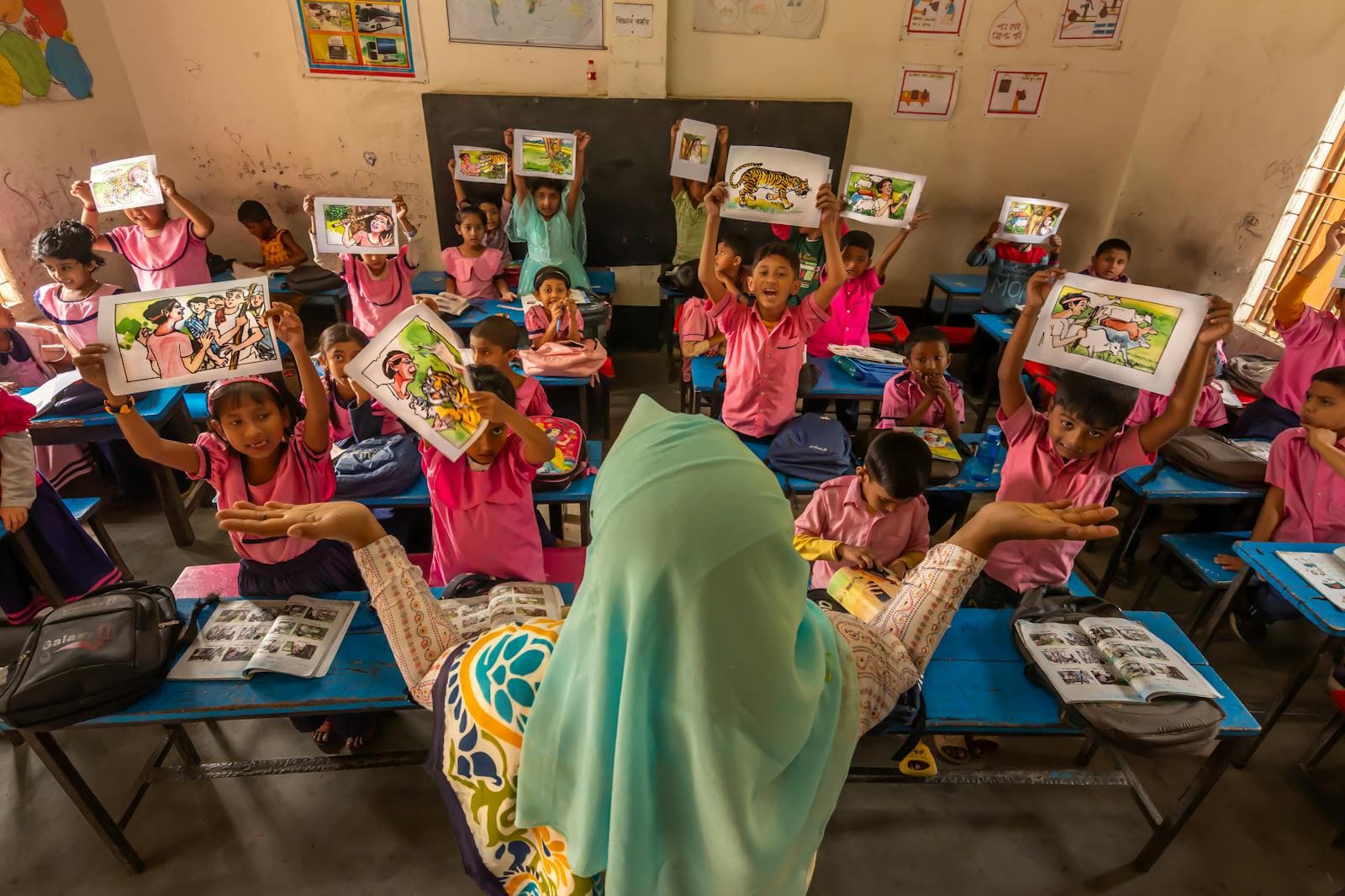 Students in a Bangladesh classroom hold up their drawings beside their teacher
