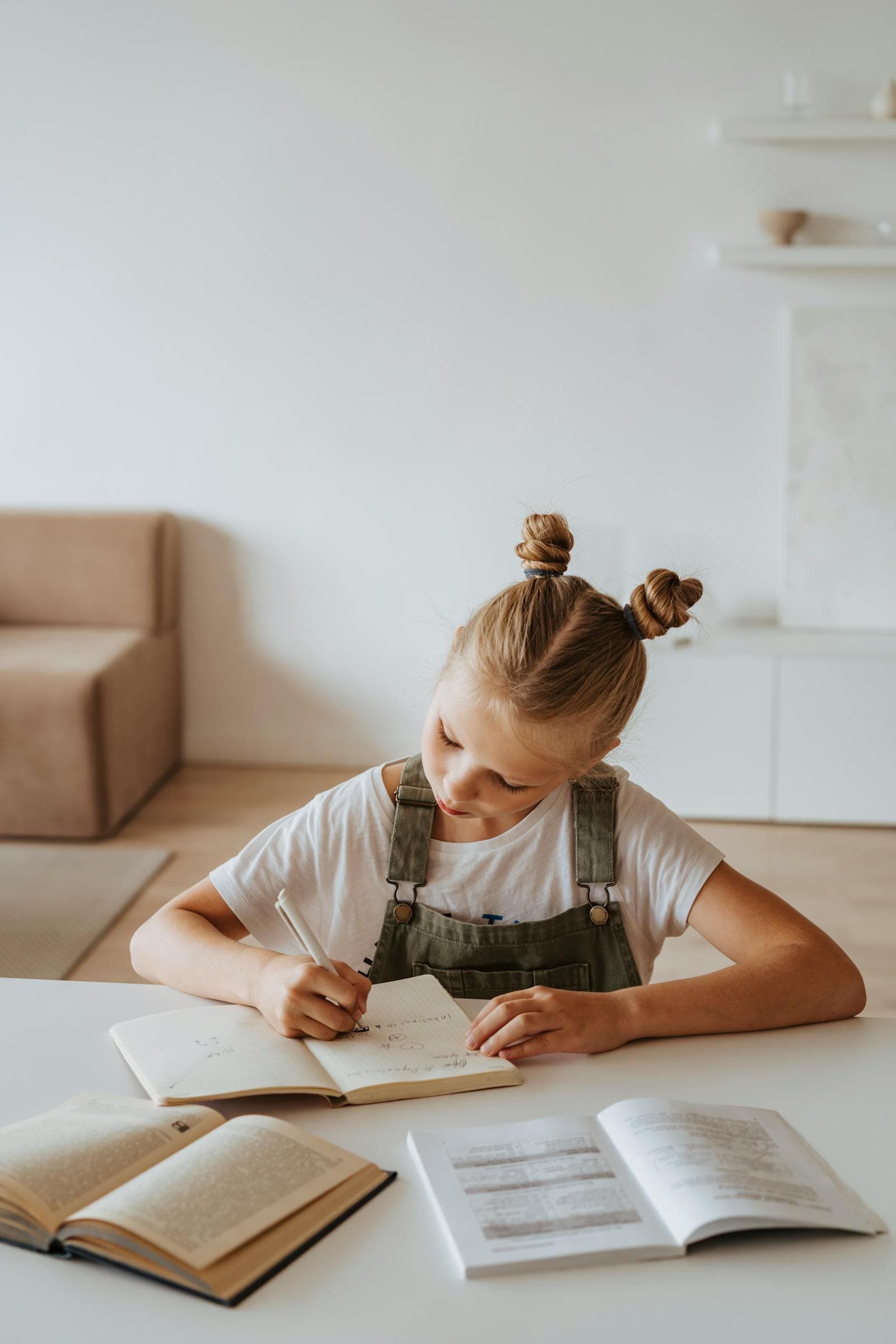 A young girl writes in her notebook with books open around her